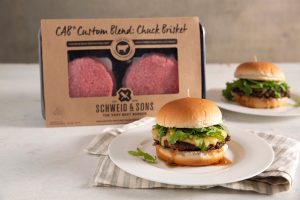 Two hamburgers cooked and ready to serve on plates, in front of a C.A.B. blend package.