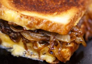 closeup of sizzling patty with onions and cheese between toasted bread.