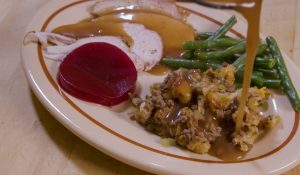 Gravy poured on top of stuffing next to green beans, turkey, and sliced beet served on a plate.