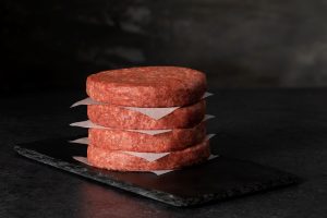 Four uncooked beef patties divided by paper setting on a black plate.