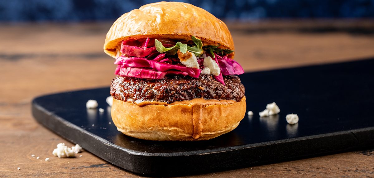 Burger on a big bun topped with bright red cabbage on a black plate.