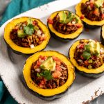 Cooked ground beef in scooped out acorn squash with 6 on a tray and topped with avocado and tomato