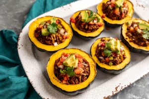 Cooked ground beef in scooped out acorn squash with 6 on a tray and topped with avocado and tomato