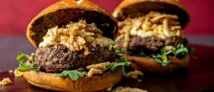 Two Burgers with fried onions on top with a maroon background