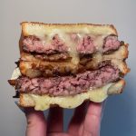A cheesy patty melt that is cut in half and stacked on top of eachother.