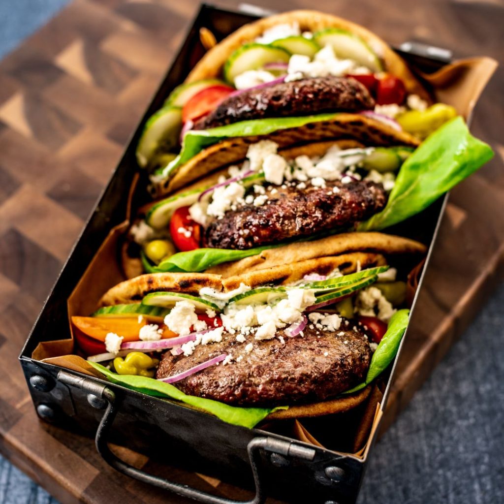 the mediterranean burger topped with feta cheese, pepperoncini, cucumbers and red onions