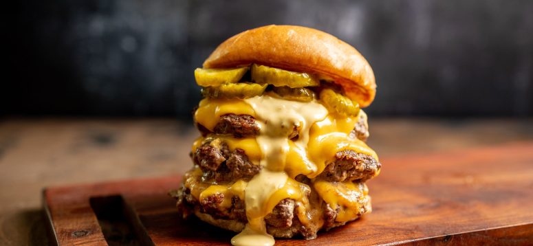 find the top burger trends, including smashburgers, in this schweid and sons blog. Pictured is a triple smashburger with cheese, pickles, and sauce