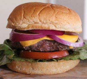 schweid and sons burger topped with tomato, lettuce, cheese, and red onions on a bun