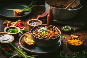 bowl of ground beef chili made with quality schweid and sons ground beef. topped with shredded cheese, jalapenos, red peppers, onions, and corn crisps