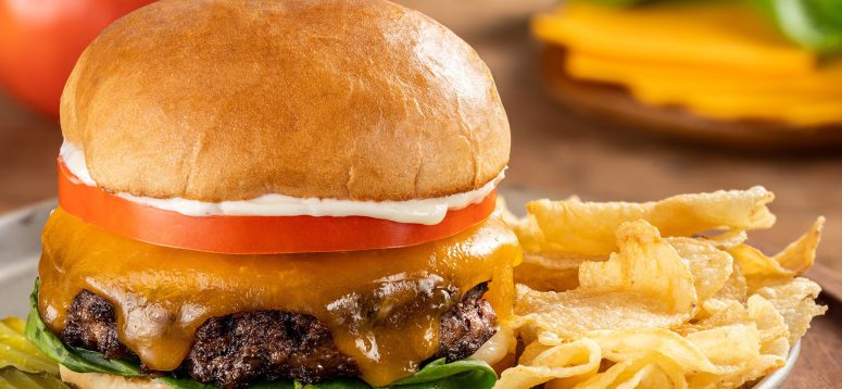 Classic cheeseburger topped with tomato, lettuce, cheddar cheese, and mayonnaise with a side of potato chips