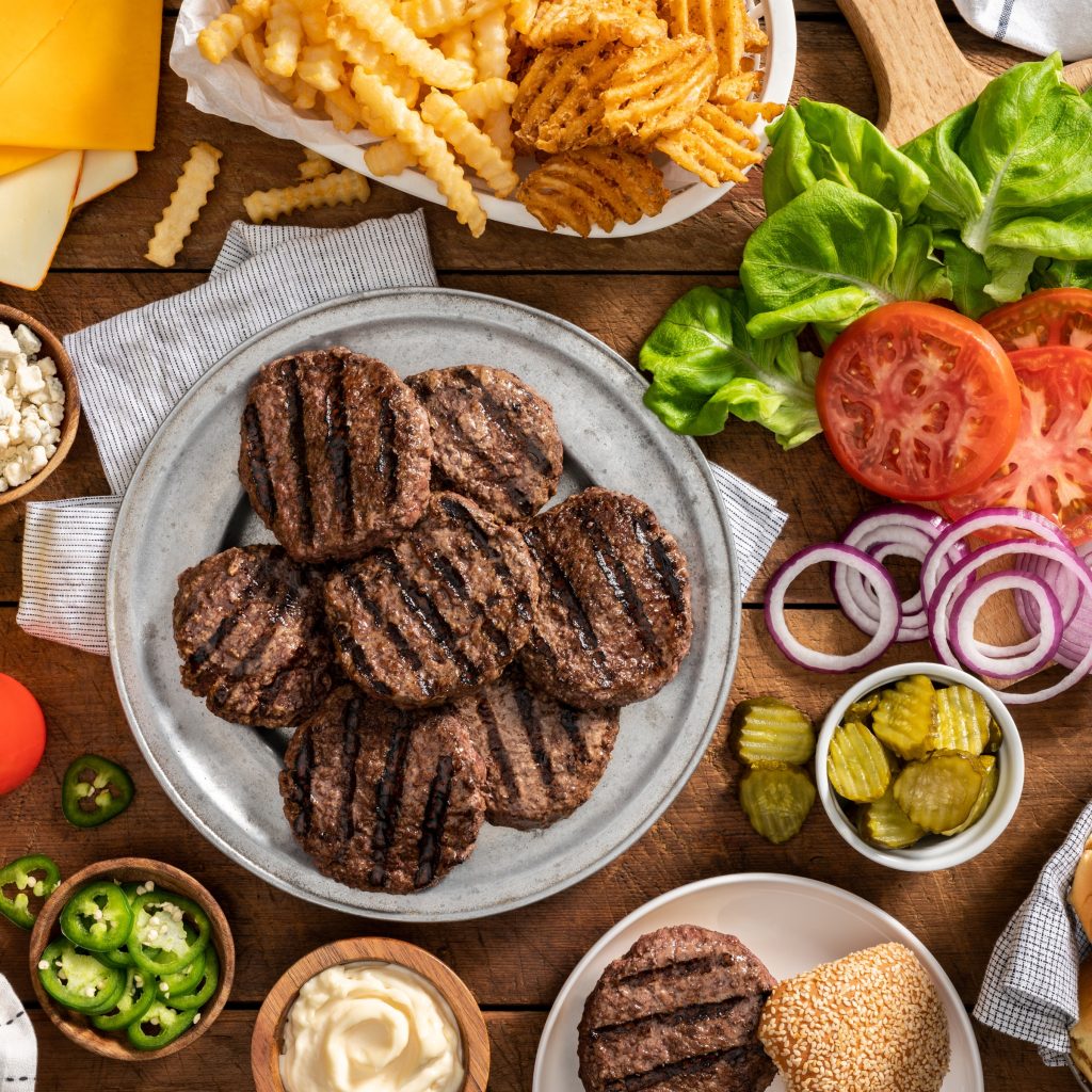 Grilled burgers with prepared toppings. Sliced onions, tomatoes, pickles, cheese