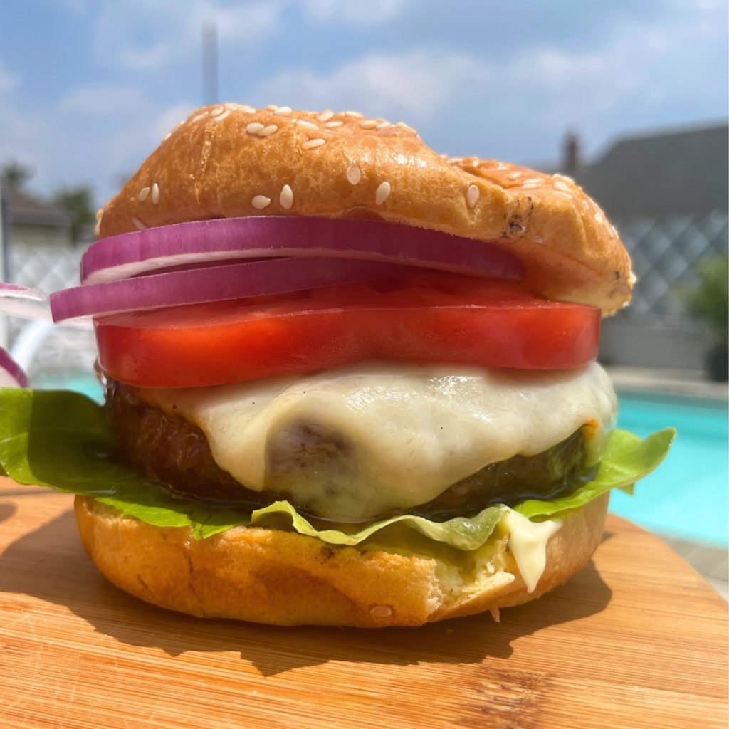 poolside burger made with schweid and sons ground beef, red onions, sliced tomato, cheese, and lettuce all on a toasted bun.