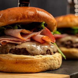Schweid & Sons burger on a brioche bun topped with leafy greens, thinly sliced ham, swiss cheese, and a dijon sauce