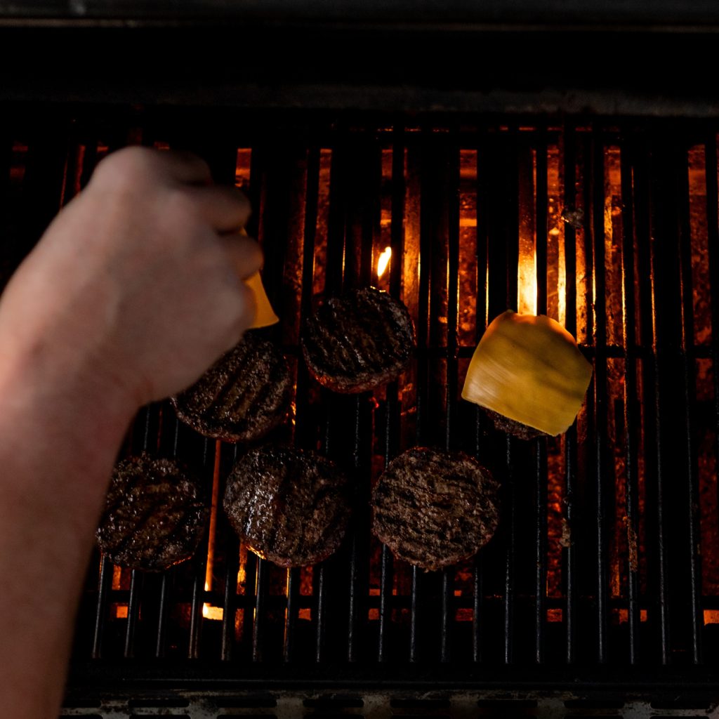 simply seasoned burgers on a grill where two are topped with cheese