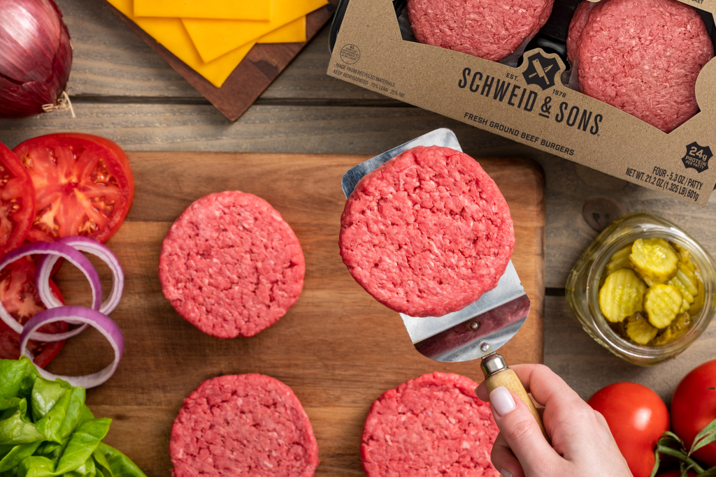 raw schweid and sons burgers surrounded by lettuce, onions, tomatoes, and pickles