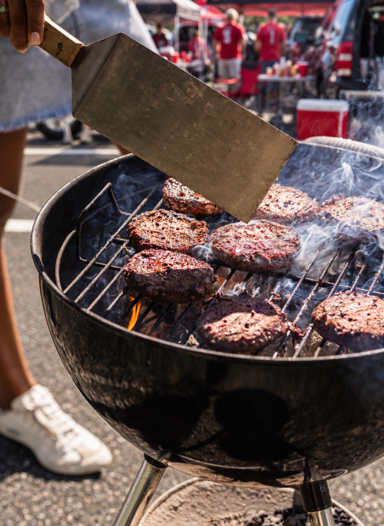 Person grilling Burgers at a football tailgate in a parking lot