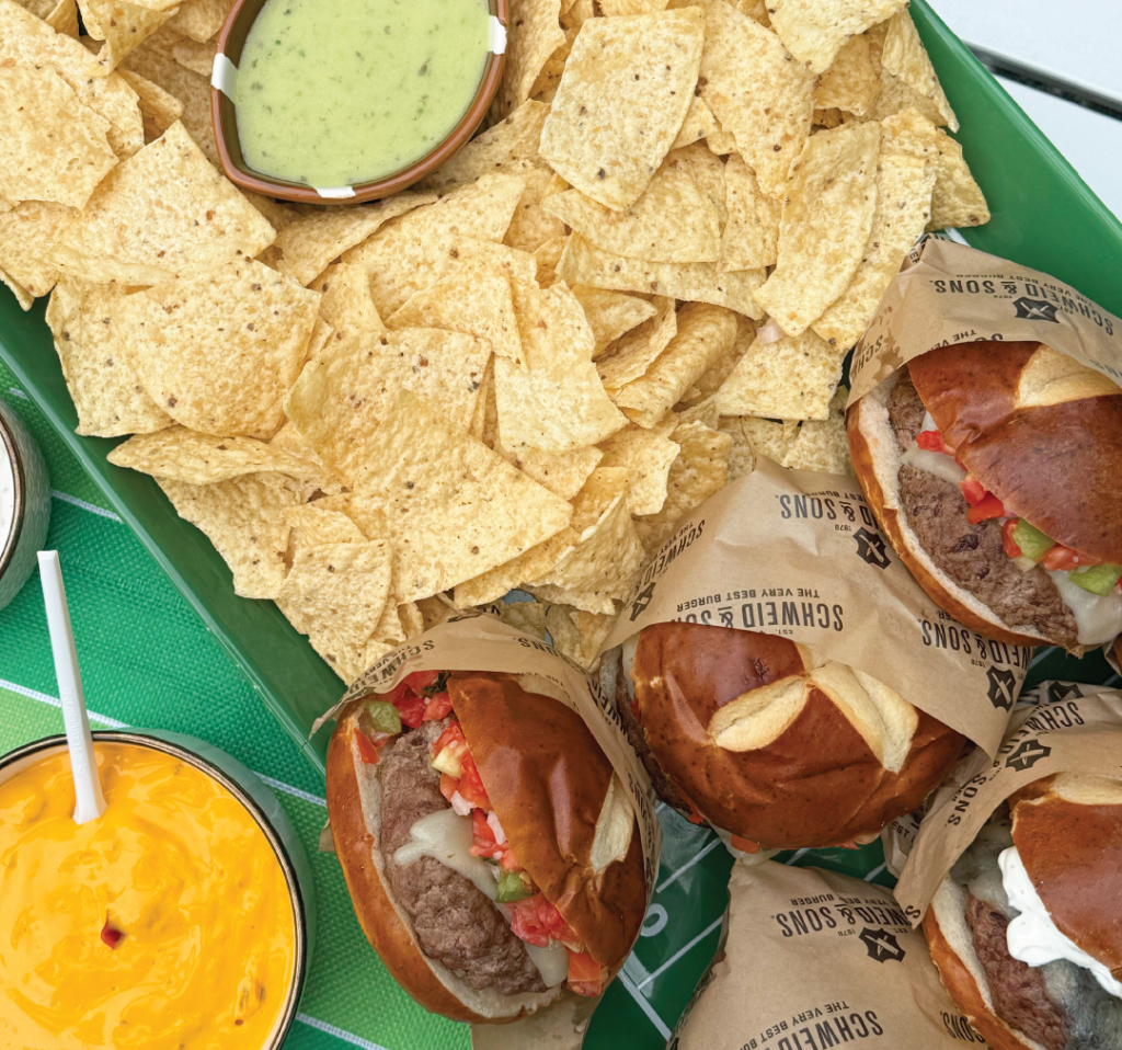 Schweid and sons burgers topped with melted cheese, pico, all on a pretzel bun served with chips and guacamole perfect for a game day spread