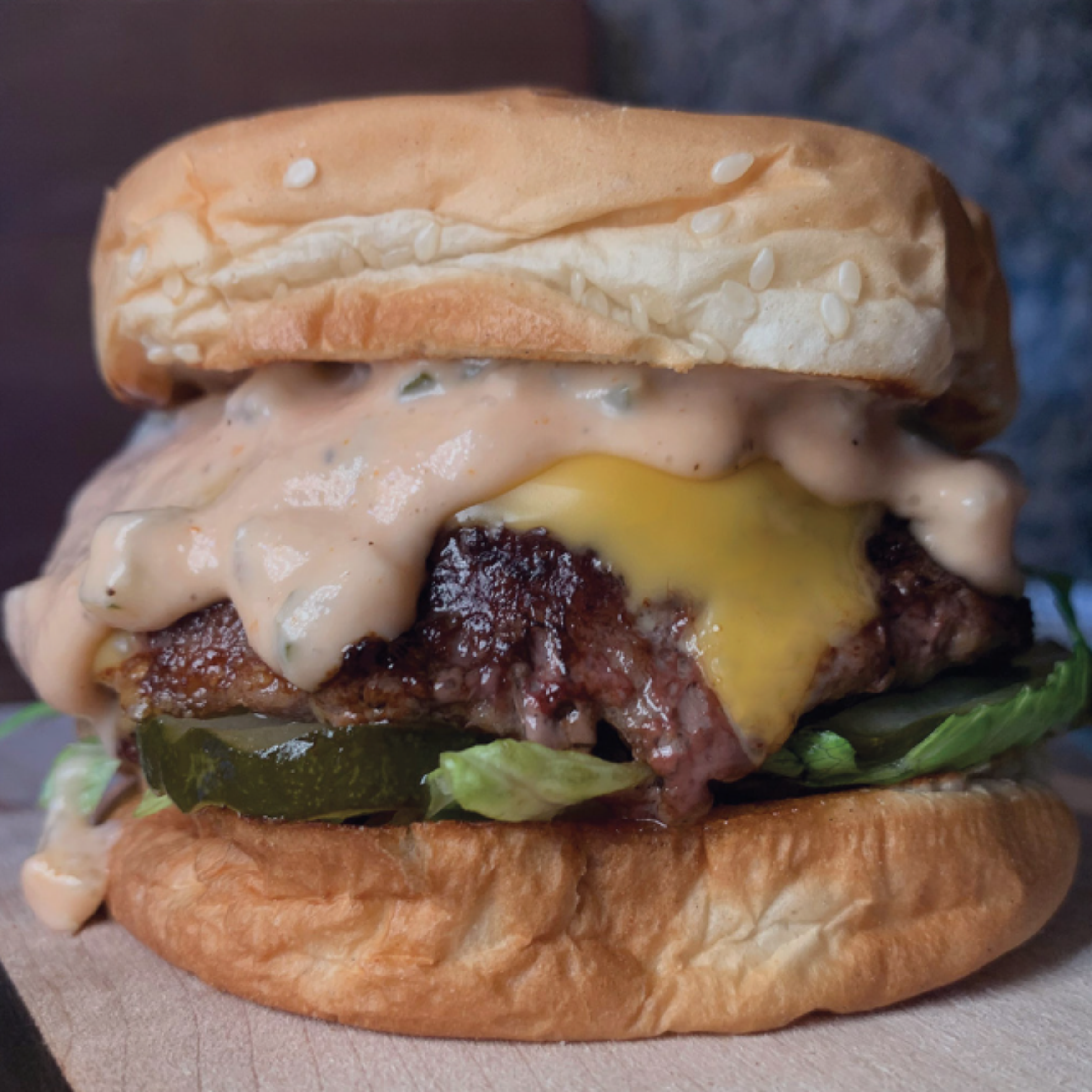 Schweid and sons burger on a sesame seed bun topped with pickles, lettuce, cheese, and dripping with sauce