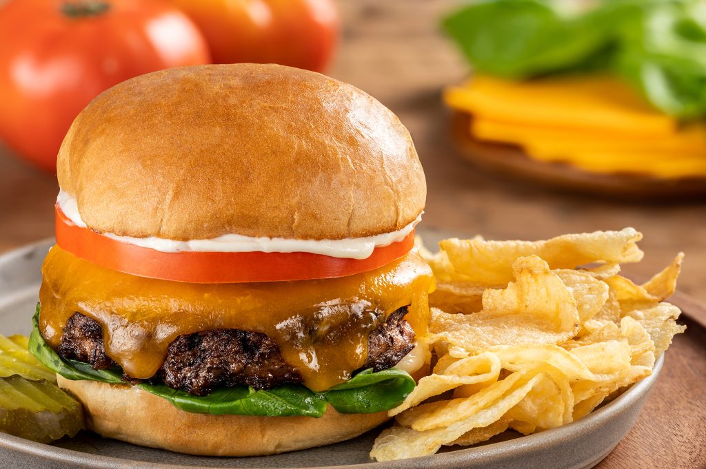 schweid and sons cheeseburger topped with lettuce, tomato, and mayo with a side of potato chips